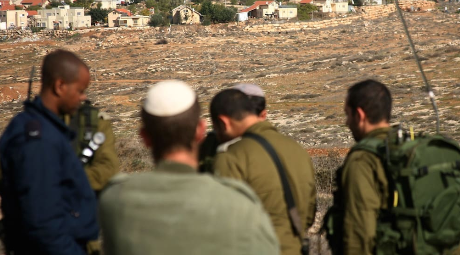 مستوطنات إسرائيلية في الضفة الغربية تظهر في الخلفية بينما يقف جنود إسرائيليون قرب أراضٍ مفتوحة