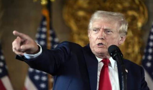 الرئيس الأمريكي دونالد ترامب يشير بيده أثناء إلقاء خطاب رسمي وخلفه أعلام الولايات المتحدة