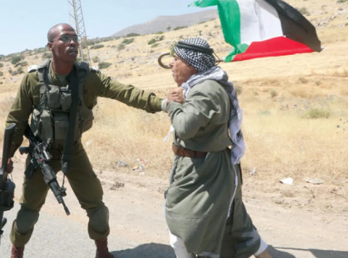 جندي إسرائيلي يمسك برجل فلسطيني يرتدي الكوفية خلال مواجهات في منطقة مفتوحة بالضفة الغربية
