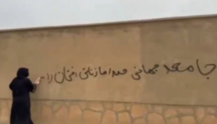 امرأة أفغانية تكتب شعارًا احتجاجيًا على جدار في مزار الشريف رفضًا لسياسات طالبان ضد النساء