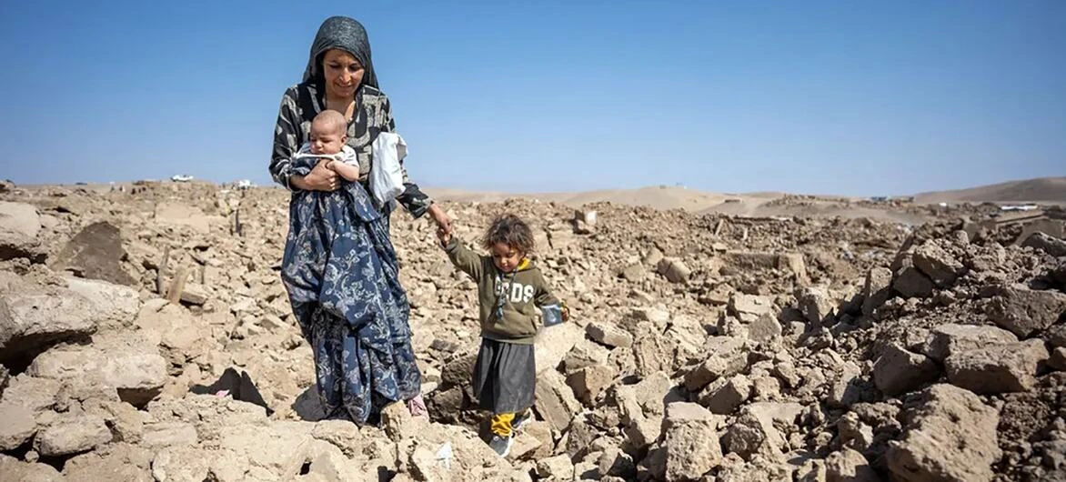 امرأة أفغانية تحمل طفلها وتسير مع طفلة وسط منطقة مدمرة